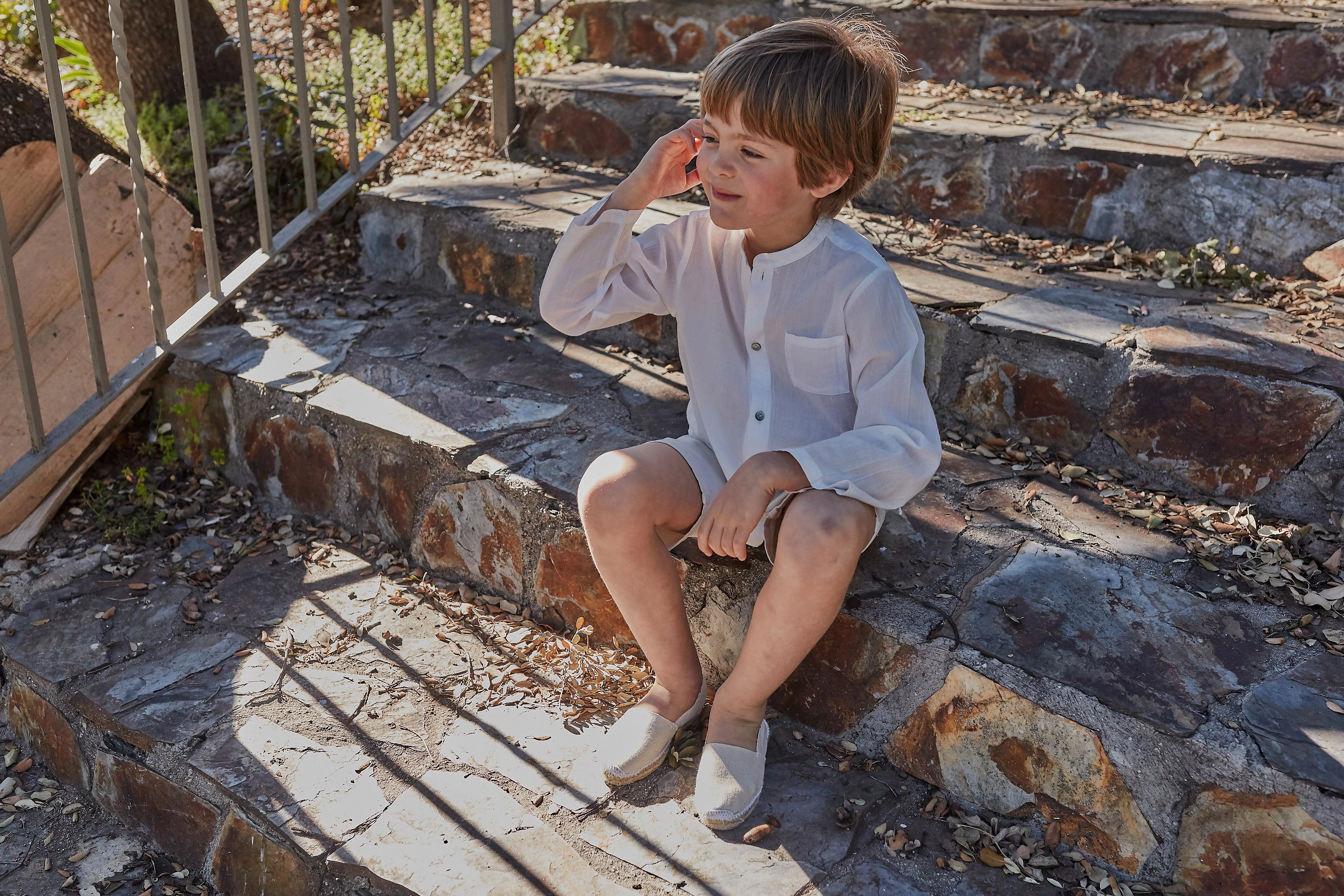 Child sitting on stone steps outdoors wearing a white outfit.