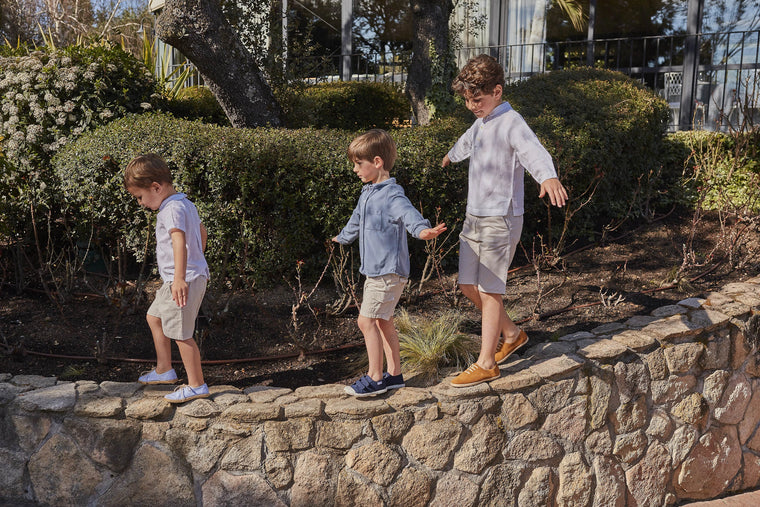 Three children playing on a stone wall with bushes and trees in the background