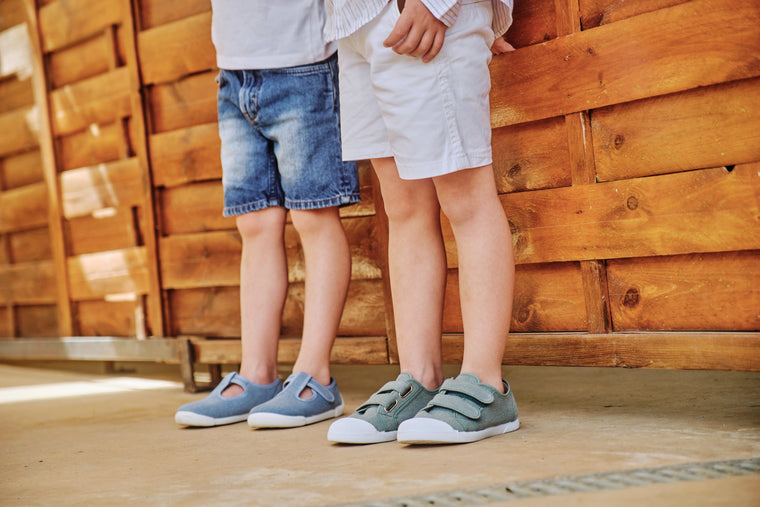 Two children standing side by side wearing matching gray shoes against a wooden background