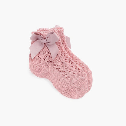 Pink knitted baby sock with a bow on a white background