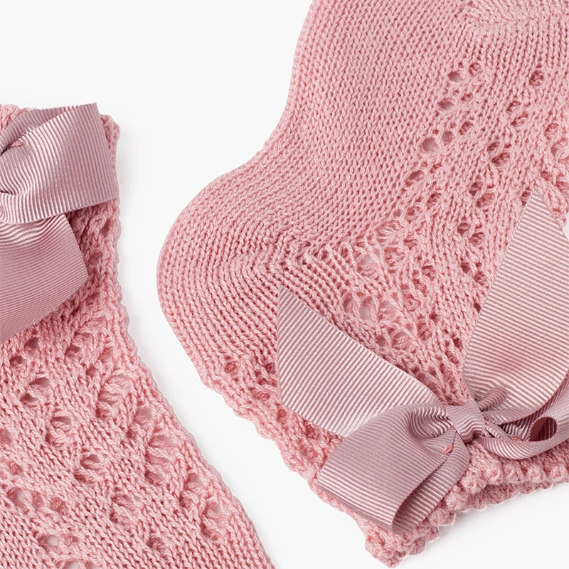 Pink knitted baby booties with ribbons on a white background