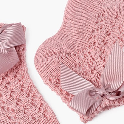 Pink knitted baby booties with ribbons on a white background